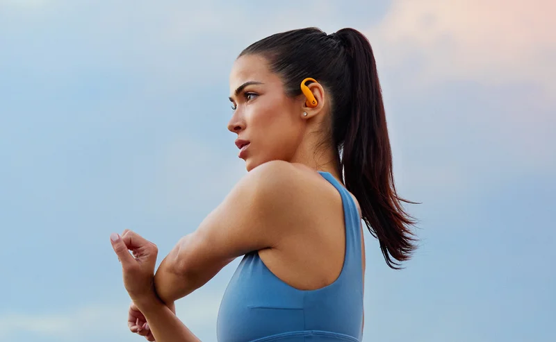 Woman wearing Powerbeats Pro 2 in Electric Orange, ready to workout outside.