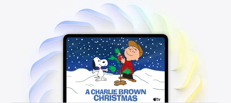 iPad Pro, 11-inch, silver color, on-screen Charlie Brown decorates small Christmas tree, Snoopy watches, snow falls, and Apple TV logo in bottom right corner, multiple angled squares with rounded corners in blue color, green color, and yellow color fan out from behind