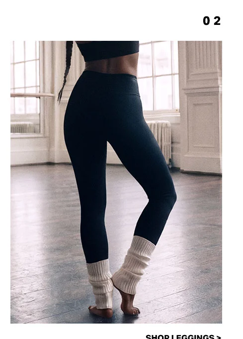 Athlete wearing black high-waisted leggings and cream leg warmers in a dance studio. Ideal comfortable yoga pants and athletic wear. Shop now.