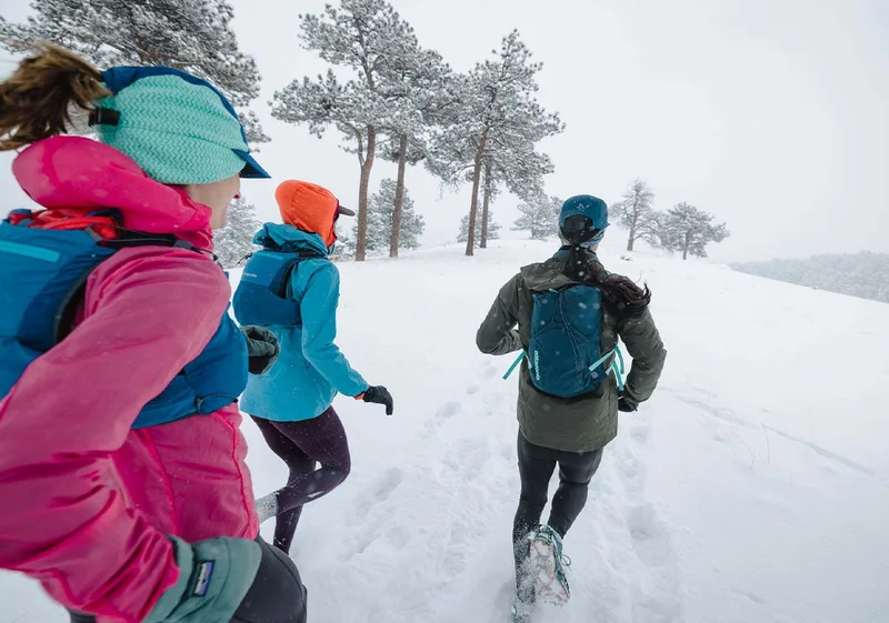 Three people running on a trail covered in snow.