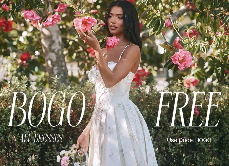 Woman wearing a white floral print spring dress, surrounded by pink garden flowers. discount code FREE on all dresses – use code discount code.