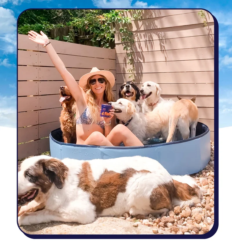 UGC image of woman in a back yard in kiddie pool surrounded by 6 dogs. Her arm is raised up and she's holding a tin of Finn Multi Vitamin.