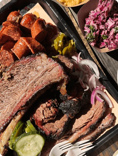 Image Description: A platter of barbecued beef brisket, sliced spicy sausages, and a side of onions