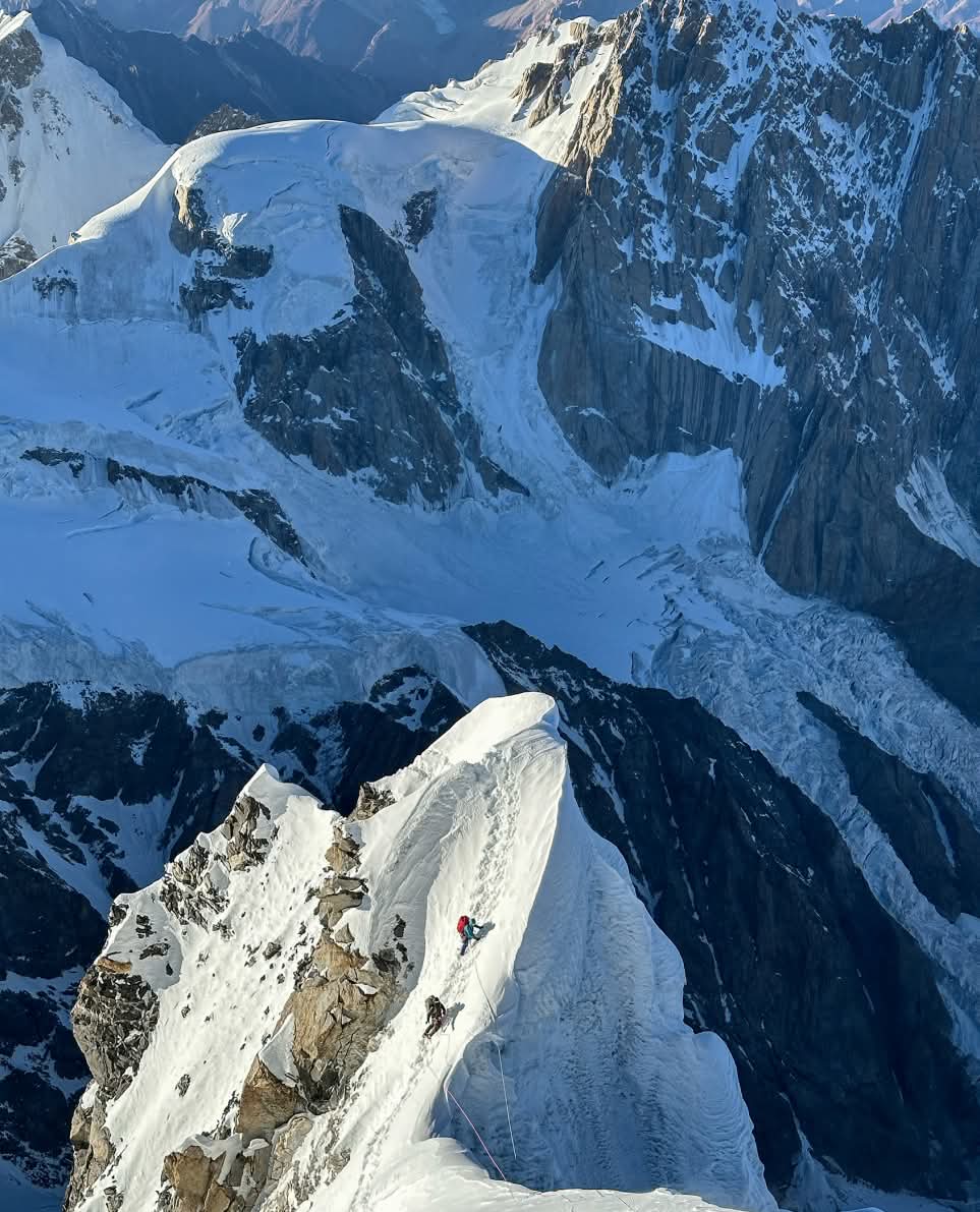Two climbers traverse a snowy ridge at high elevation.