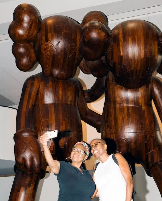 Two friends take a photograph with “Along the Way” by KAWS