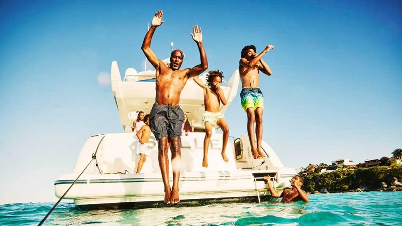 Image description: Wide shot of father and sons jumping into water from swim deck of yacht during family vacation in Caribbean Sea.