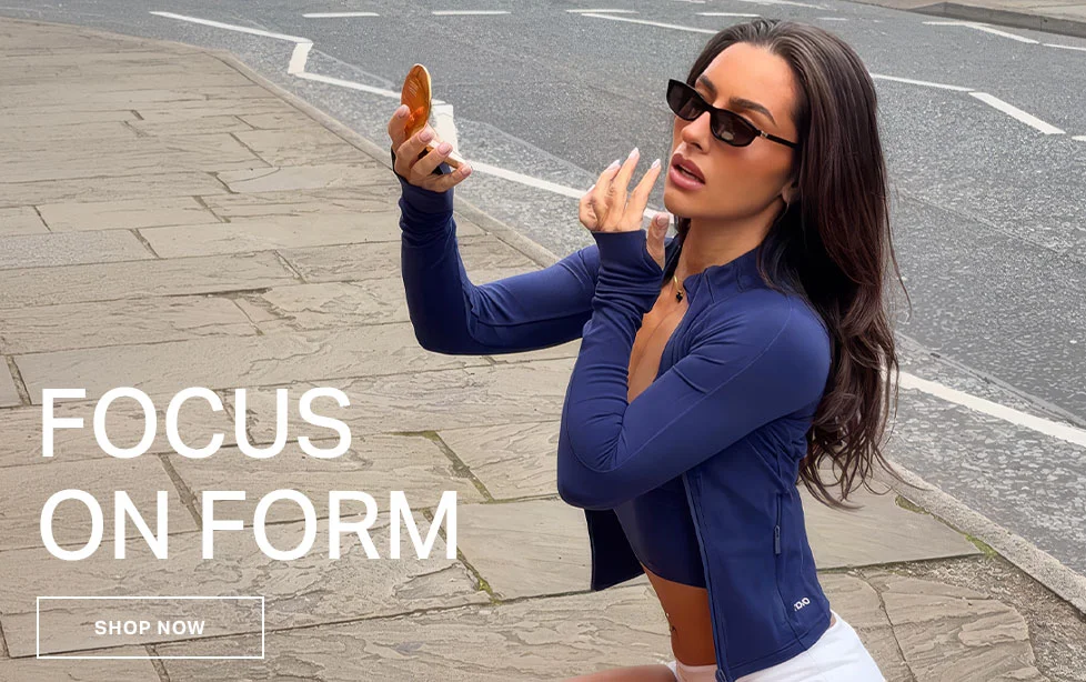 Stylish woman in navy long-sleeve activewear top & white shorts checking reflection. Shop high-performance gym wear & athleisure.