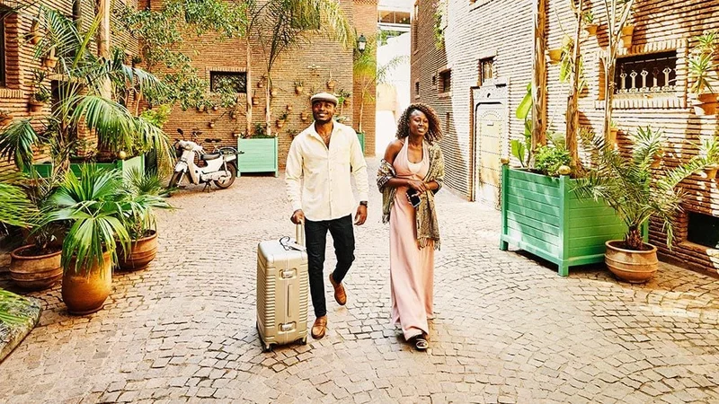 Image description: A couple walking down cobblestone street with suitcase