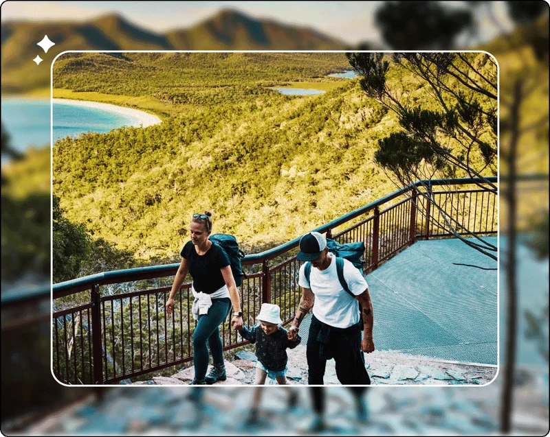 Image Description: Family hiking up a paved trail with green hills and small lakes in the background. The woman and man both hold hands with the child in the middle.