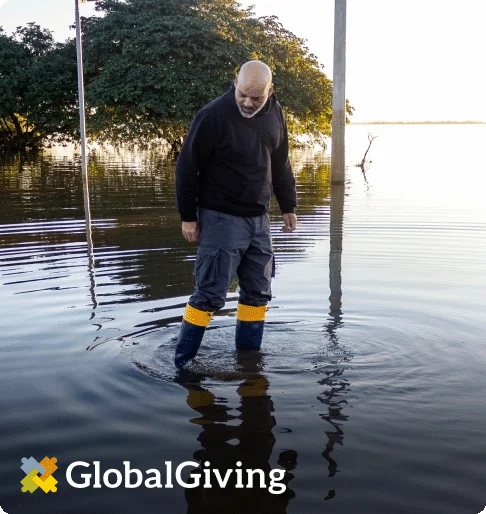 Image Description: A man wearing rain boots wades through flood water that is up to his shins.