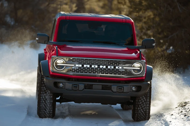 A Ford Bronco® SUV being driven across snow while its wheels kick up snow behind it.