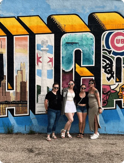 Image Description: A group of travelers posing in front of the famous Greetings From Chicago mural