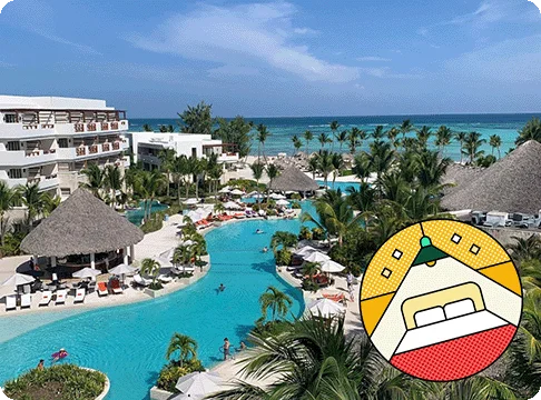 Image Description: A beach resort with a large pool surrounded by palm trees. A Hotel Explorer badge is on the bottom right corner of the image.