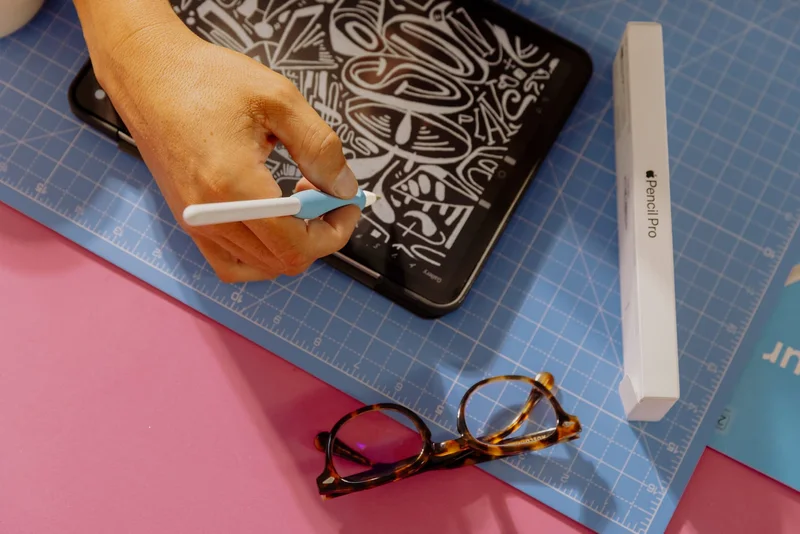 A hand drawing on an iPad with an Apple Pencil with the Apple Pencil Pro box and glasses sitting next to it.