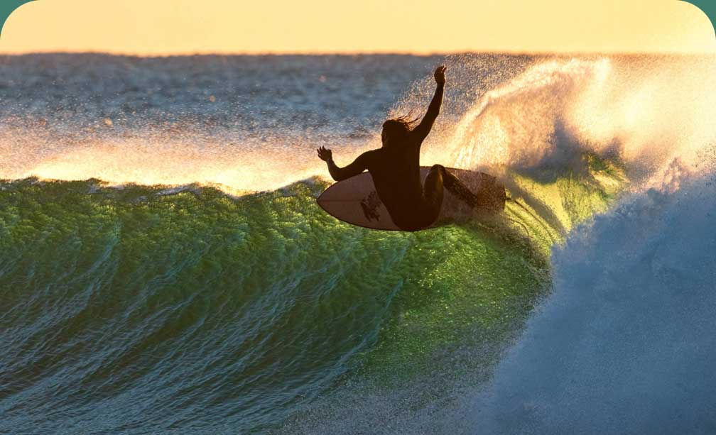 A surfer makes a critical top turn on a backlit wave.