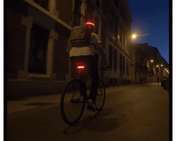 Rear view of a cyclist riding through a quiet street at night, highlighted by a glowing red tail light.
