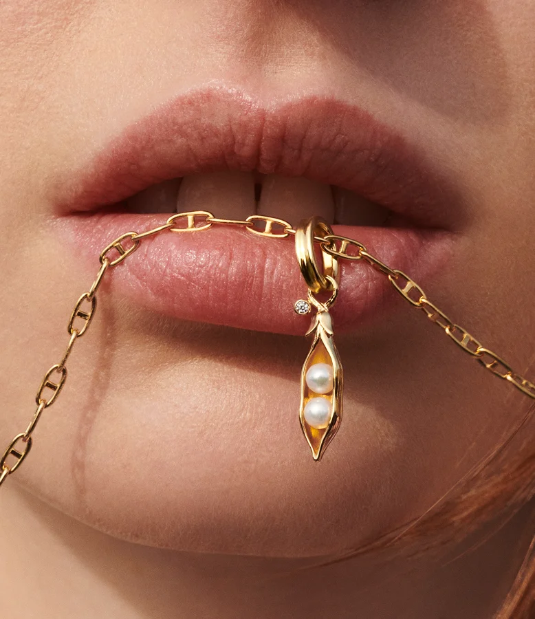 Close up of a model biting a necklace chain with a pea pod charm