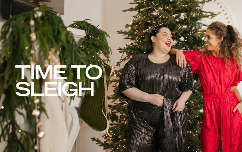 2 brunette models wearing shiny rompers next to christmas tree and fireplace with text 'time to sleigh'