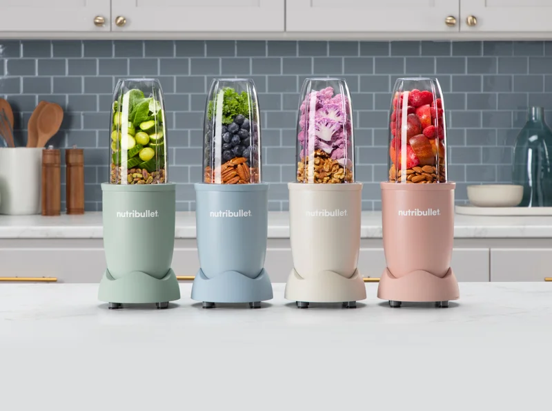 Group of four nutribullet blenders on countertop with various nuts, fruits and vegetables.