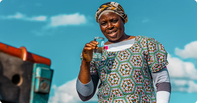 A woman smiling at the camera as she holds a glass of clean water.