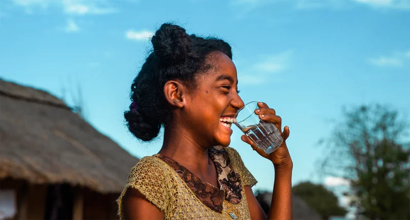 A young girl smiling as she drinks a glass of clean water.