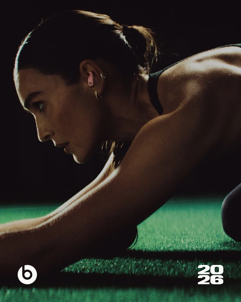 Kirsty Godso, wearing Power Pink Powerbeats&nbsp;Fit earbuds, leans forward in a focused pose on a green turf.