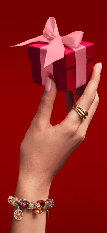 A hand holding a Pandora gift box and wearing a charm bracelet A hand holding a Pandora gift box and wearing a charm bracelet