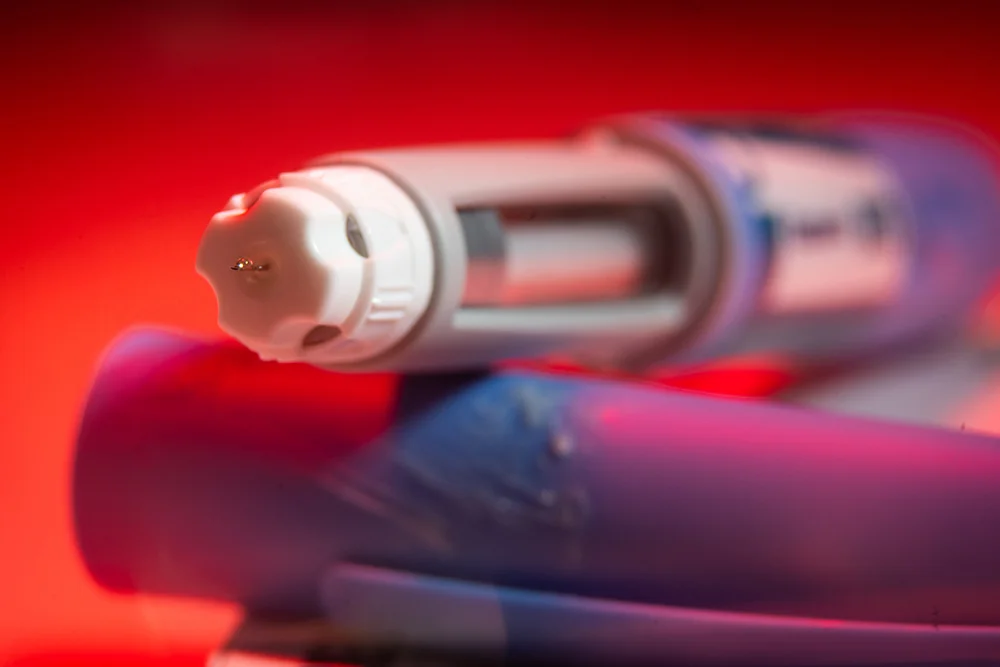 An Ozempic needle injection pen photographed against a red background.