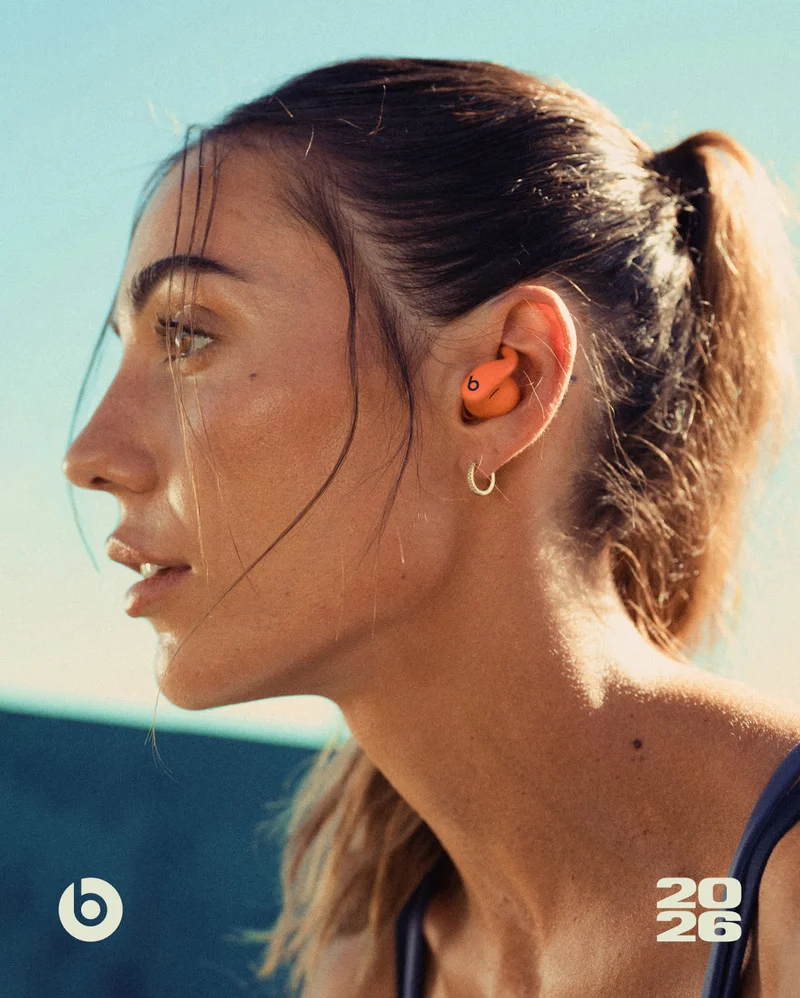 Sami Clarke wears orange Powerbeats&nbsp;Fit earbuds, looking forward with a bright blue sky in the background.