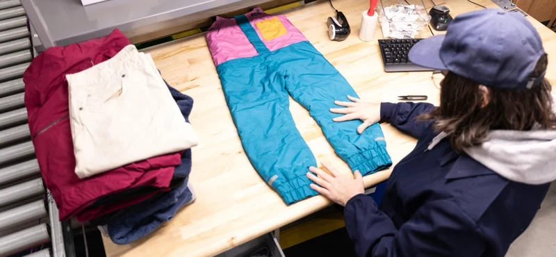 A person assesses a repaired garment laid flat on a table.