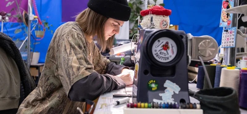 A person sits at a sewing machine and repairs a garment.
