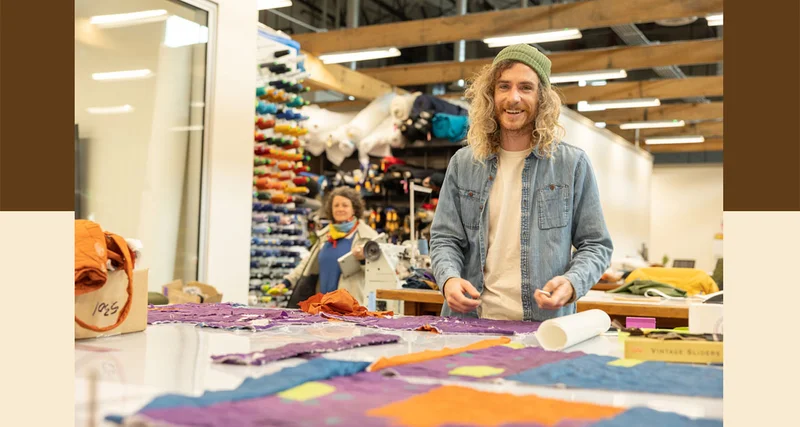 A Patagonia prototype engineer smiles while standing beside a table covered with fabric scraps.