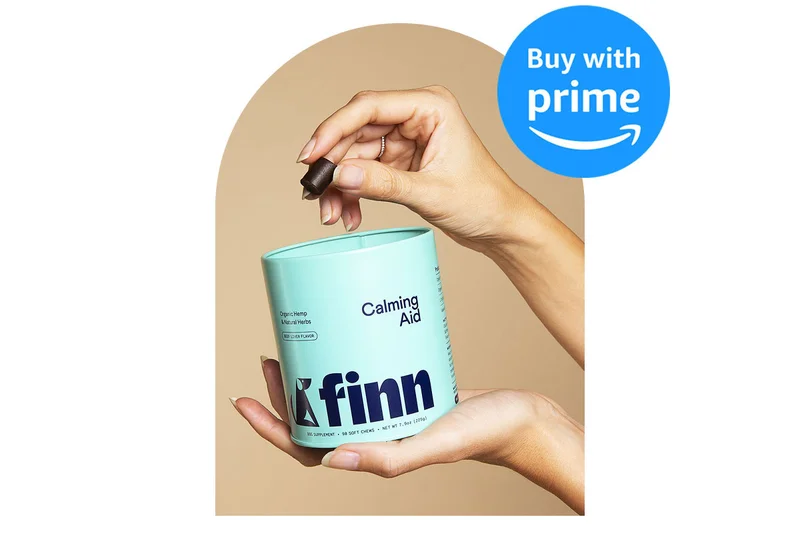 Image of hand pulling a soft chew out of a Calming Aid tin against a beige seamless backdrop. A badge reads "Buy with Prime"