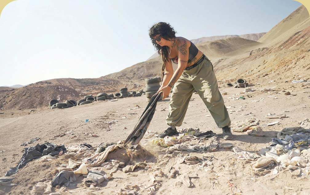 A person pulls discarded clothes from a trash pile in the desert.
