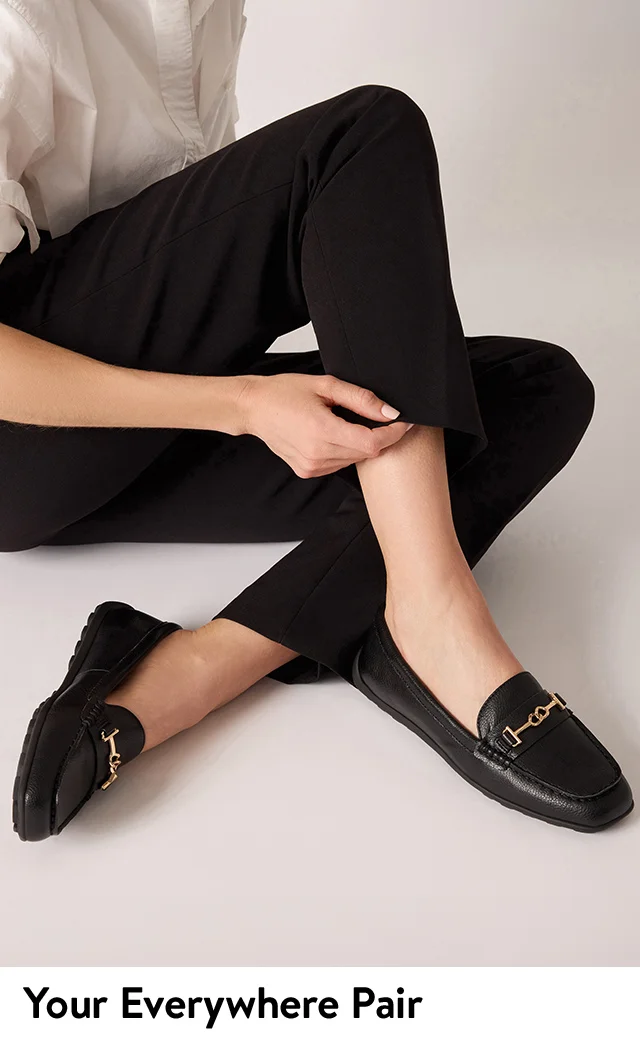 A woman wearing black loafers with gold hardware.