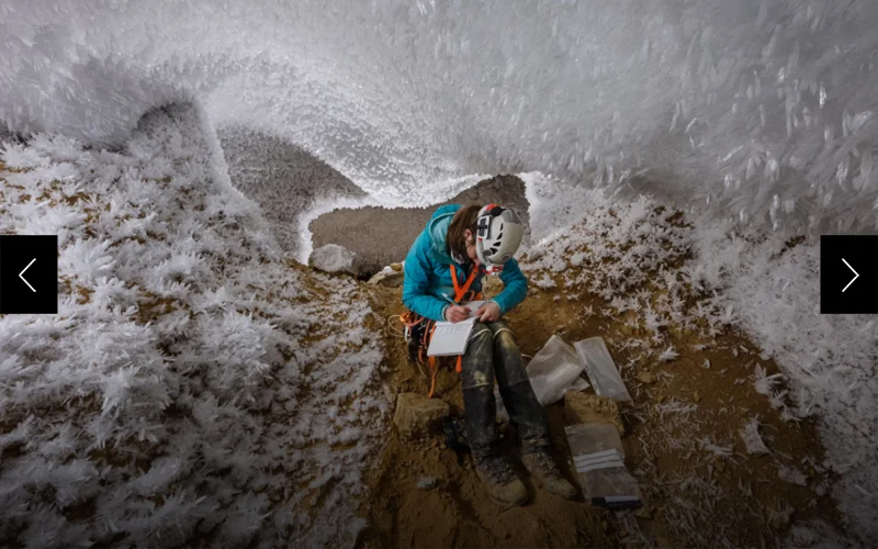 Underneath a ceiling of hoarfrost crystals and ice, a woman takes notes while sitting in a cave.