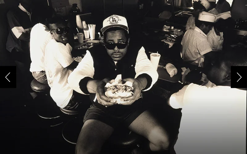 Rapper and musician Tone Loc stretches his arms toward camera, offering a half-eaten hamburger in Los Angeles in 1990.