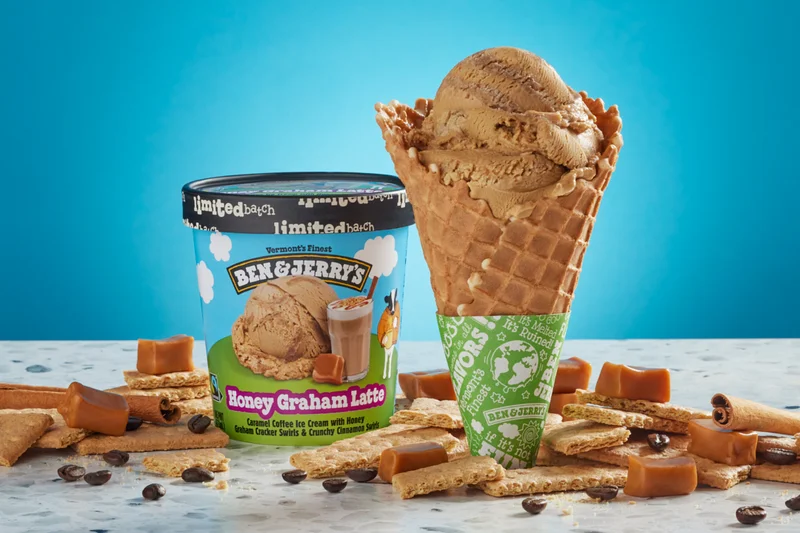 Pint of new Ben & Jerry's Honey Graham Latte ice cream next to a waffle cone of the same flavor.