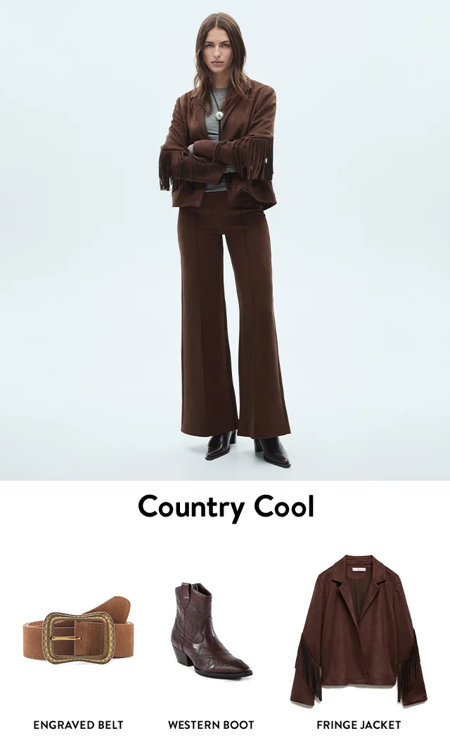 A woman wearing a brown jacket with fringe sleeves, grey top, bolo necklace and brown trousers.