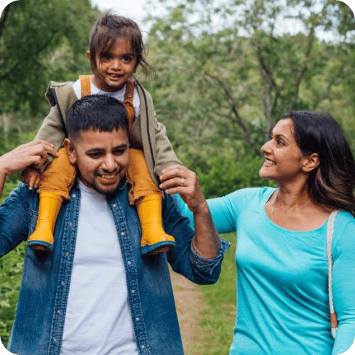 a dad with his toddler daughter on his shoulders beside mom on a neighborhood walk a dad with his toddler daughter on his shoulders beside mom on a neighborhood walk