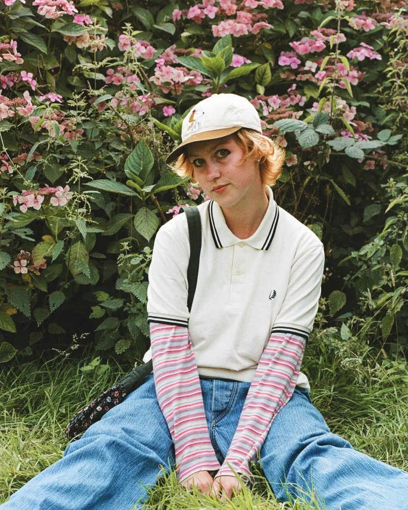 Women sitting on grass in front of pink flowers wearing a White Twin Tipped Fred Perry Shirt