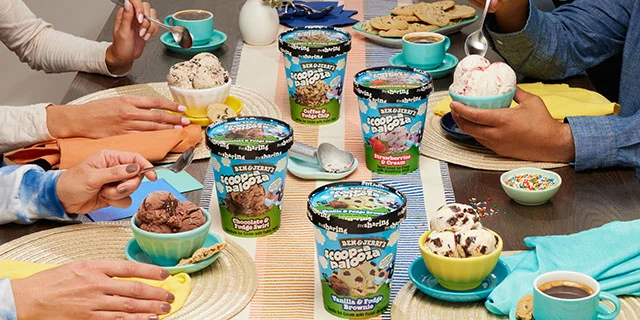 Table with people eating ice cream out of bowls. Four Ben & Jerry's Scoop-apalooza tubs are visible.
