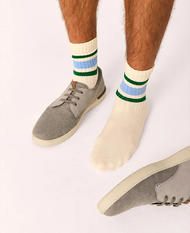 Man wearing striped gym socks with one Bear sneaker in Grey. Shop Now.
