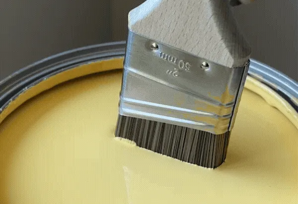 Paint brush dipping into Golden Hour yellow paint