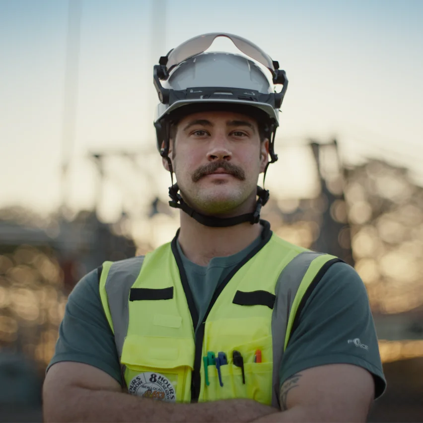 Man in a white hard hat and yellow safety vest with arms crossed.