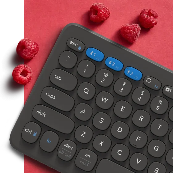 Keyboard on a light red backround surrounded by raspberries