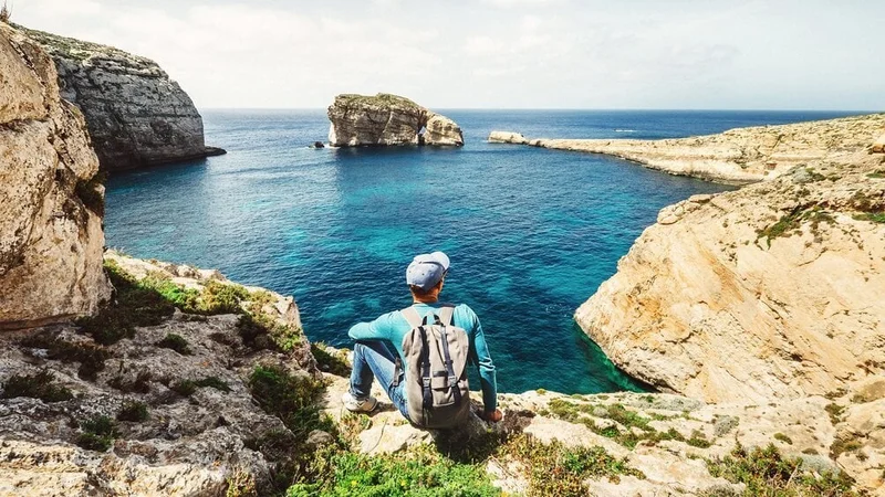 Image description: Backpacker relaxing on the rocky coast of Blue Lagoon, Malta