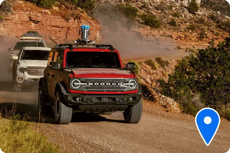 Two Ford vehicles being driven behind a red Bronco® SUV down a trail. The Bronco SUV has Google Street View™ technology attached