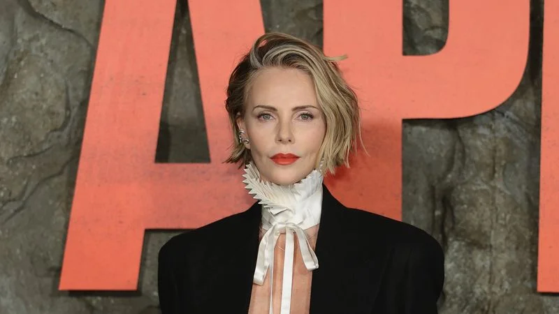 Image may contain: Charlize Theron, Blonde, Hair, Person, Formal Wear, Clothing, Coat, Suit, Blazer, Jacket, Face, and Head