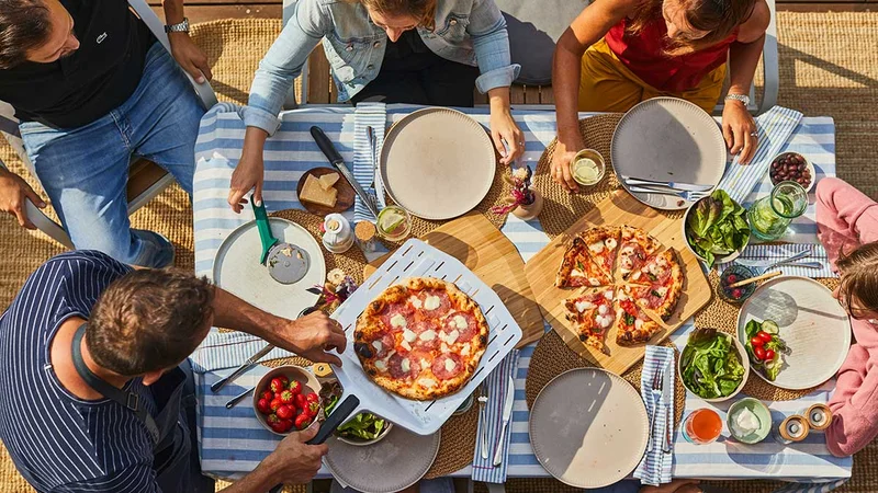 A head down shot of a table of people enjoying multiple pizzas